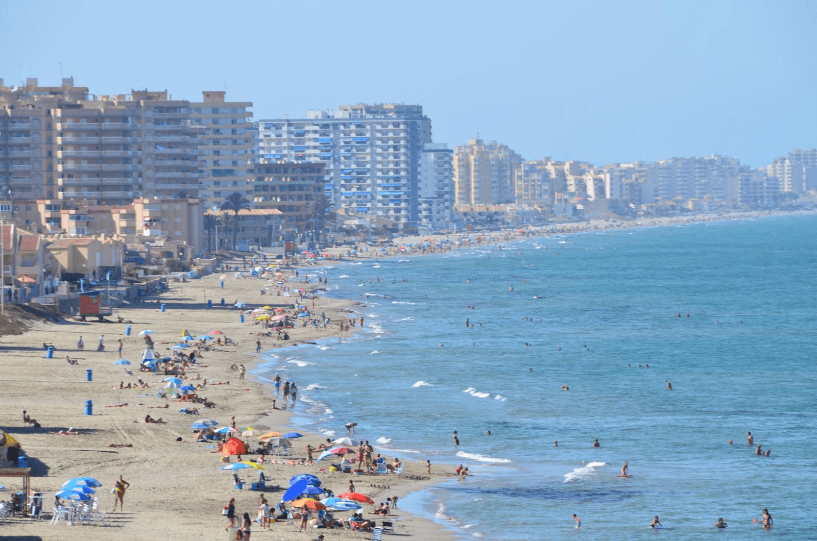 image of the beach during summer with multiple people sunbathing