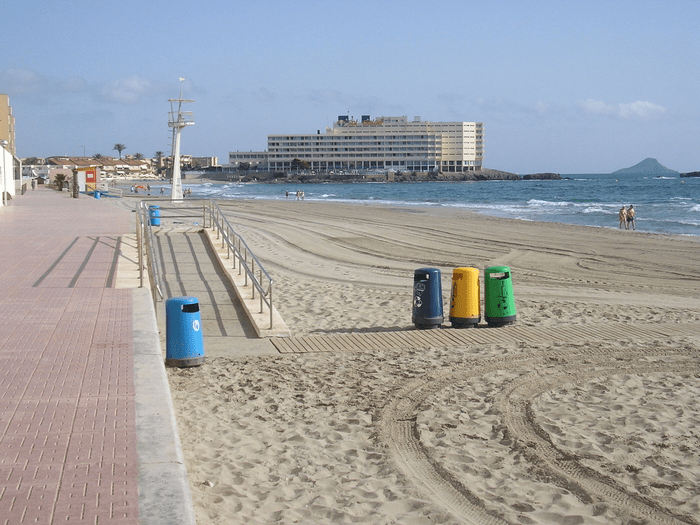 image of the beach showing trash cans and people walking on the sand